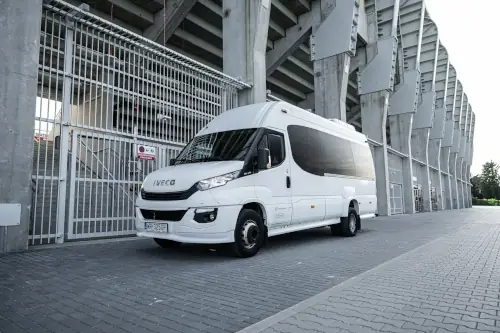 MINI_Biały Bus Iveco Ustawiony Bokiem Pod Trybuną Stadionu Obok Bramy Na Stadion Widok Horyzontalny Wynajem Autokaru Skaryszew Wynajem Autokaru Skaryszew