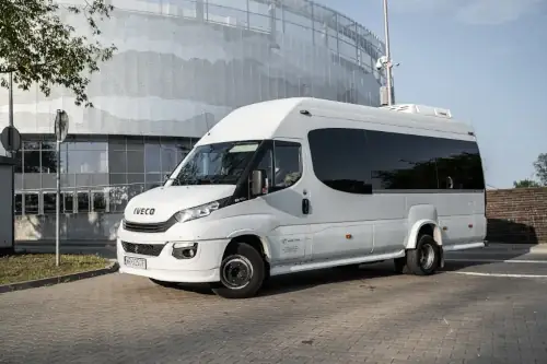 MINI_Bus Biały Czarny Premium Iveco Ustawiony Bokiem W W Tle Hala Sportowa Widok Horyzontalny Wynajem busa z kierowcą Radom Bus Biały Czarny Premium Iveco Ustawiony Bokiem W W Tle Hala Sportowa Widok Horyzontalny