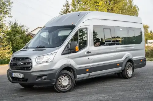 MINI_Srebrny Bus Marki Ford Transit Autobus Zdjęcie od Boku Widok Horyzontalny Wynajem busa z kierowcą Radom Bus Biały Czarny Premium Iveco Ustawiony Bokiem W W Tle Hala Sportowa Widok Horyzontalny