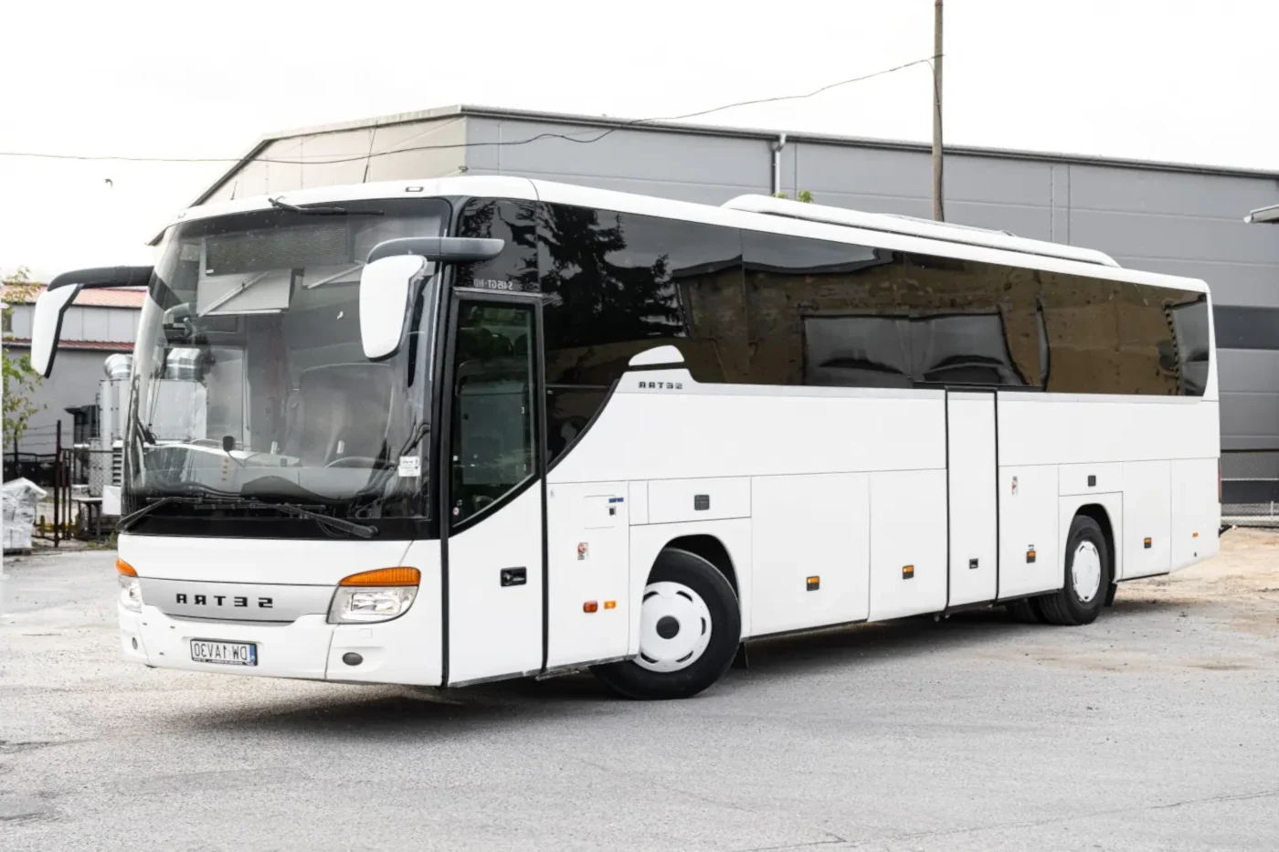 MAIN_bialy autokar turystyczny marki setra z przyciemnionymi szybami ustawiony pod katem z skreconymi kolami na industrialnym tle landscape